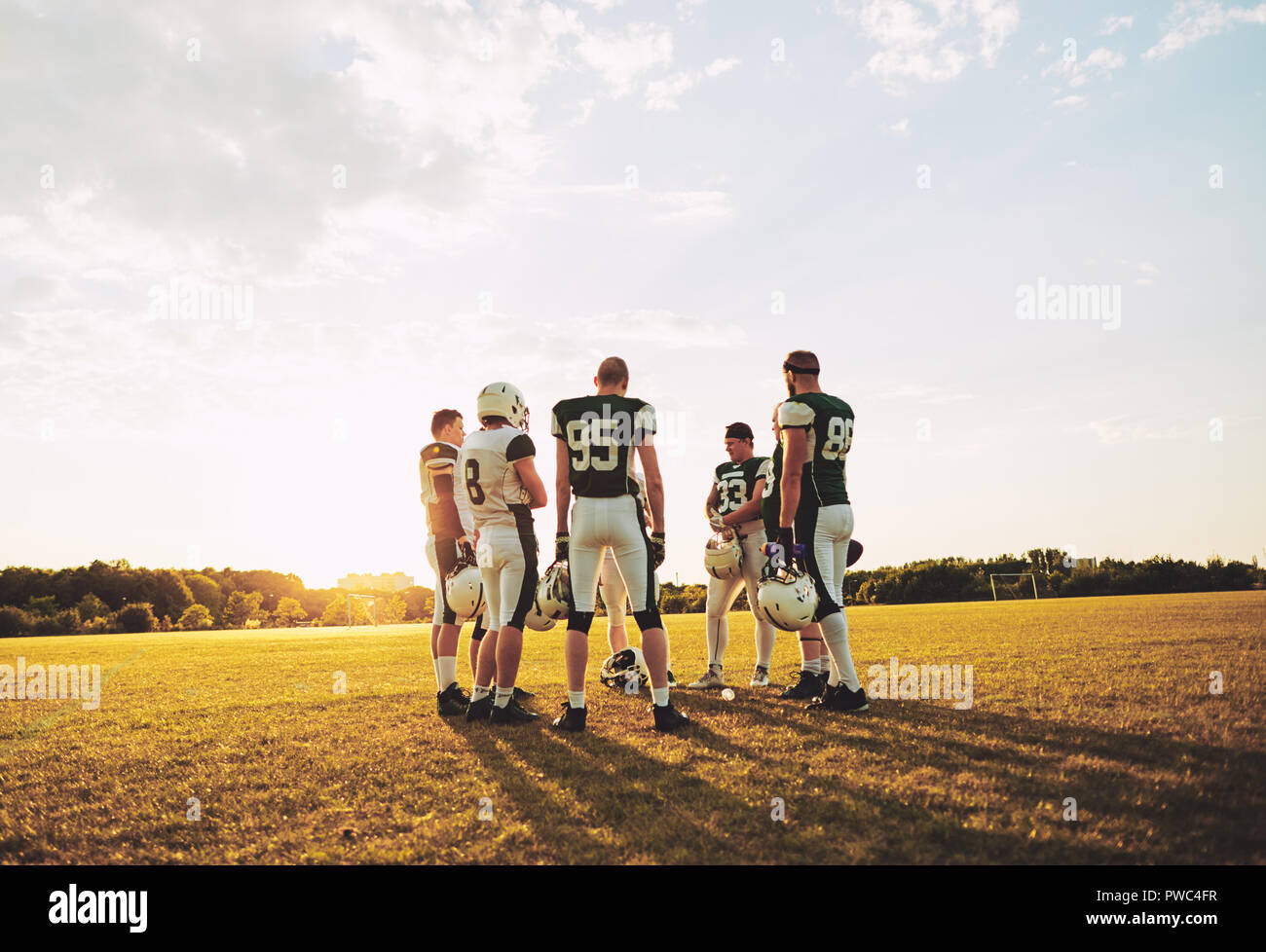Group of young American football players discussing strategy during practice while standing together on a sports field in the afternoon Stock Photo