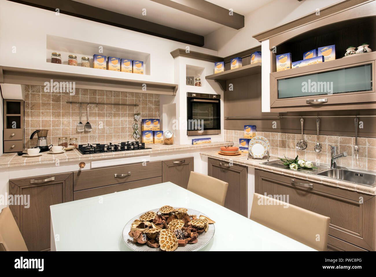 Rustic or kitchen interior with cooking supplies, built in cabinets with tiled splash back, fitted appliances and a center table with homemade cookies Stock Photo