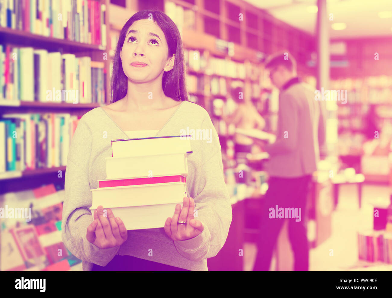 Sad young Brazilian girl holding pile of books in bookstore Stock Photo ...