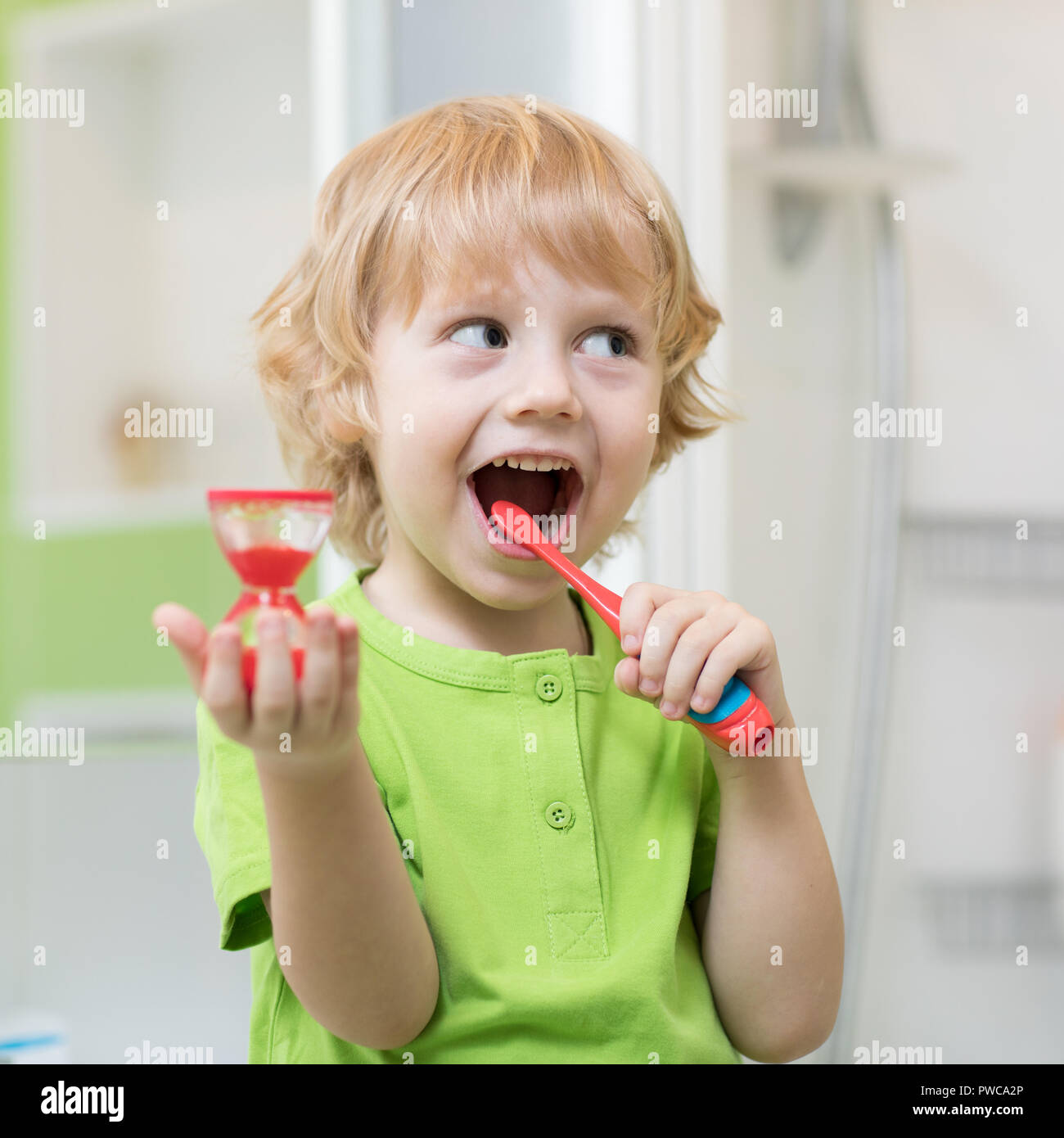 Little kid boy brushes his teeth monitoring lasting with hourglass