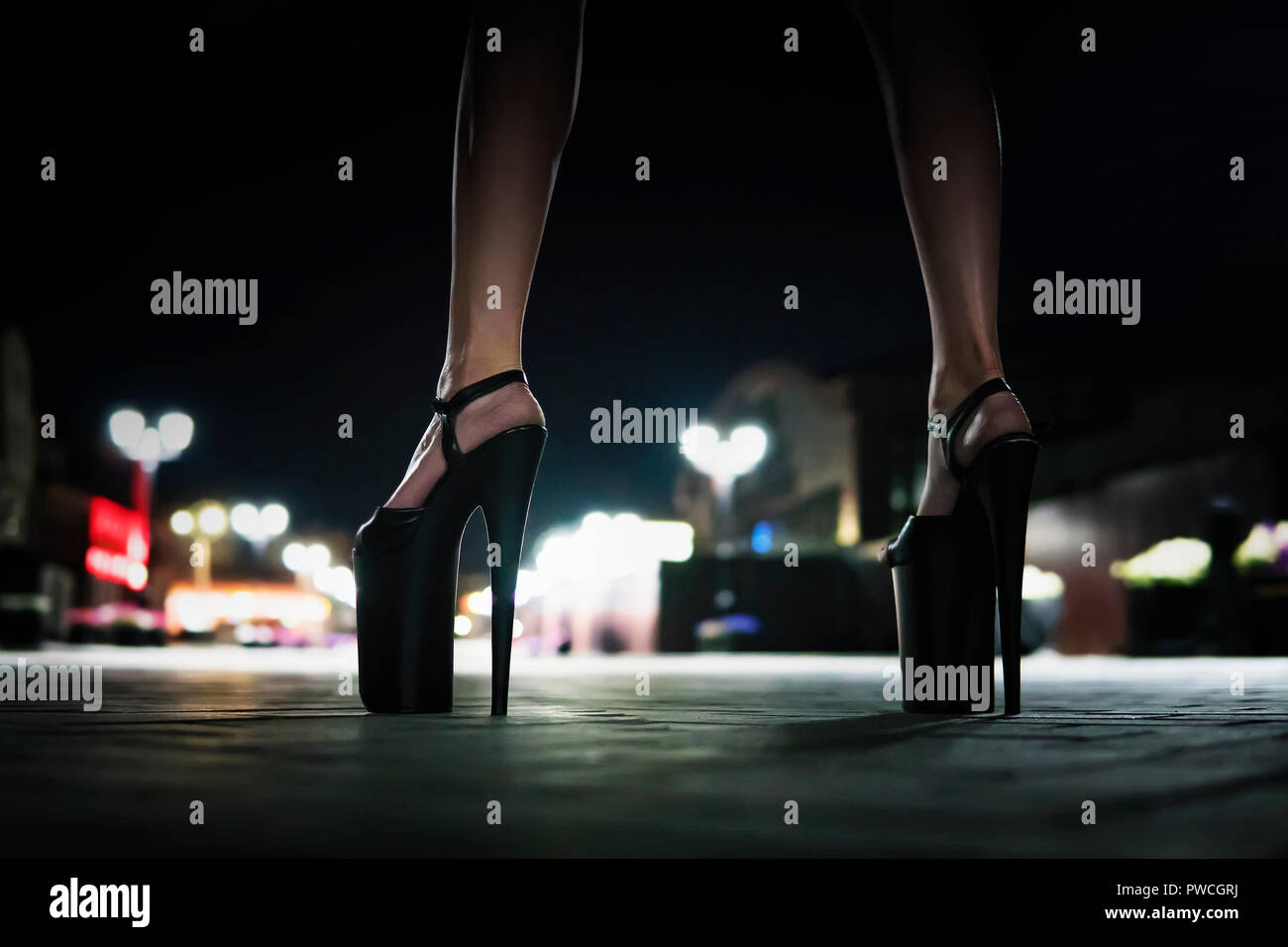 Close-up view of female legs wearing shoes on a high heel. Woman standing on the bridge in evening and waiting. High-heeled shoes for performing on st Stock Photo