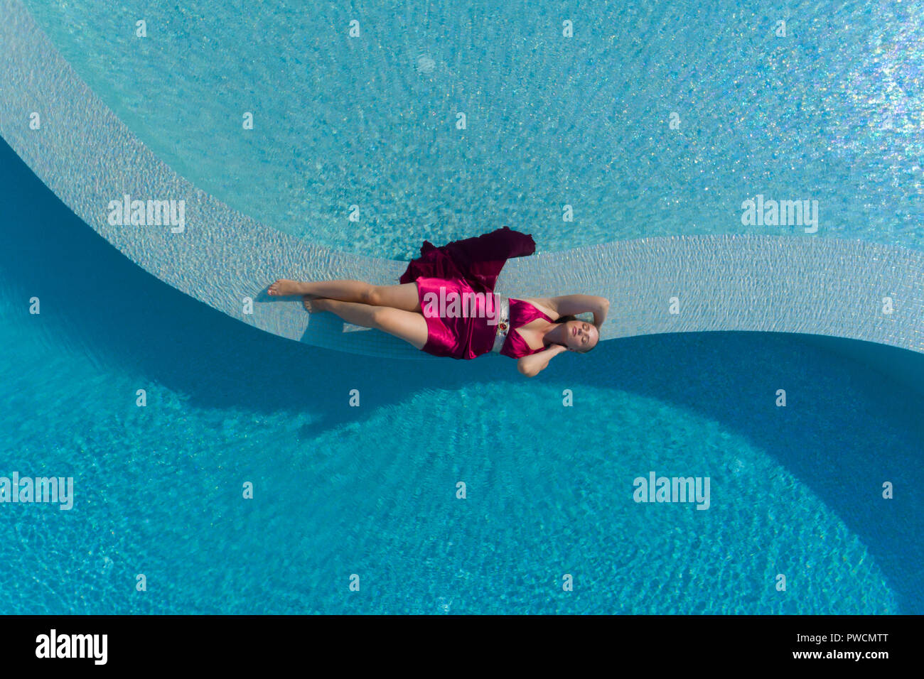 Young blonde woman in red dress lying in the swimming pool Stock Photo