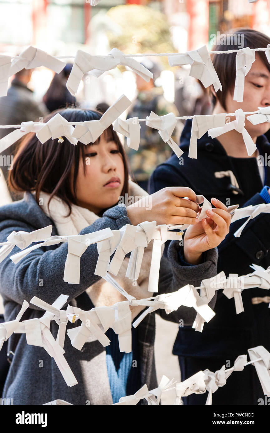 Japanese new year, shogatsu. Young woman tying bad fortune paper slip, Omikuji to framework to leave bad luck behind at the Nishinomiya shrine. Stock Photo
