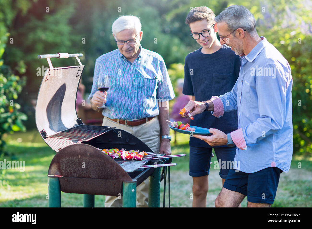 Family gathered for a bbq in the garden. men are grilling meat Stock Photo  - Alamy