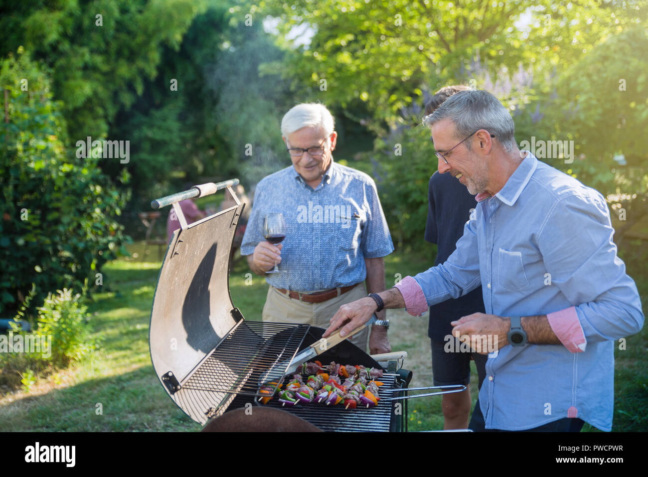 Family gathered for a bbq in the garden. men are grilling meat Stock Photo