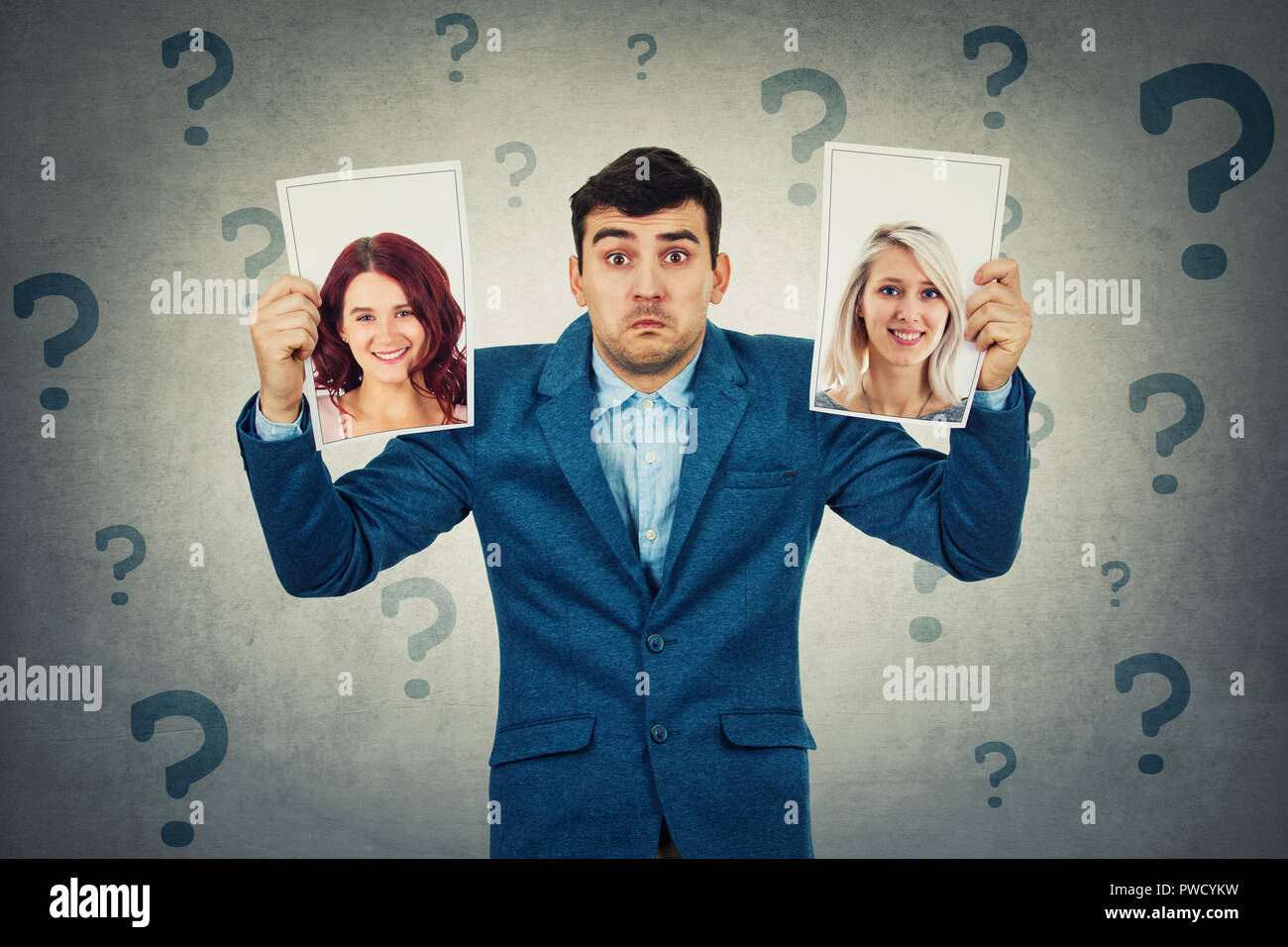 Undecided young man holding two photos has to choose between two woman, question marks around head. Girlfriend partner first date choice love and roma Stock Photo