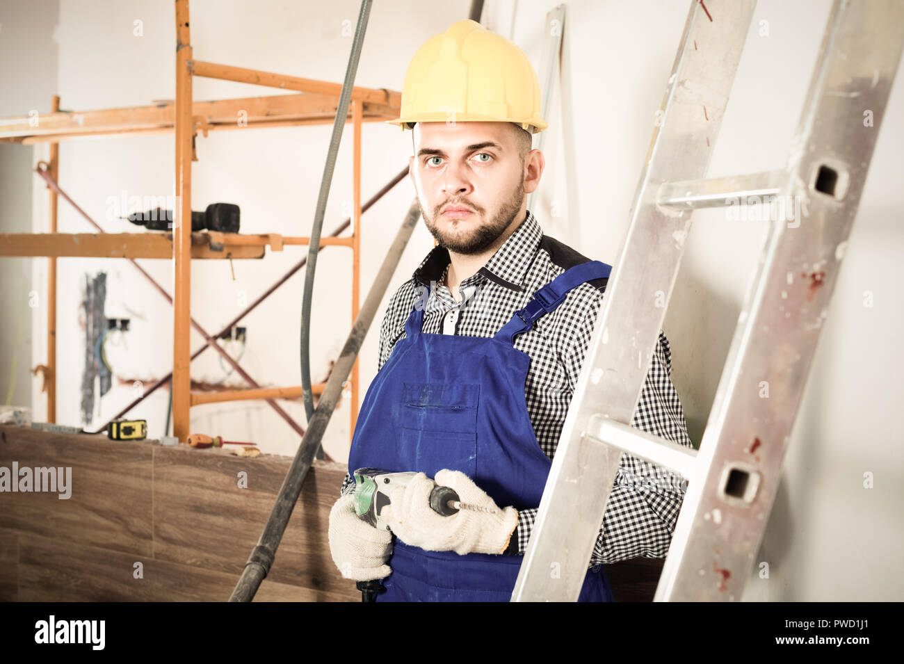 Diligent serious male worker is ready to work with a dril at the object ...