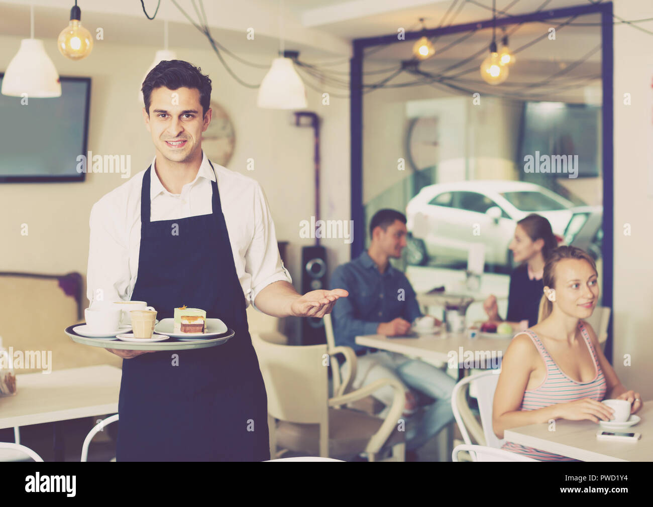 Portrait of adult hospitable waiter inviting to taste coffee and cake