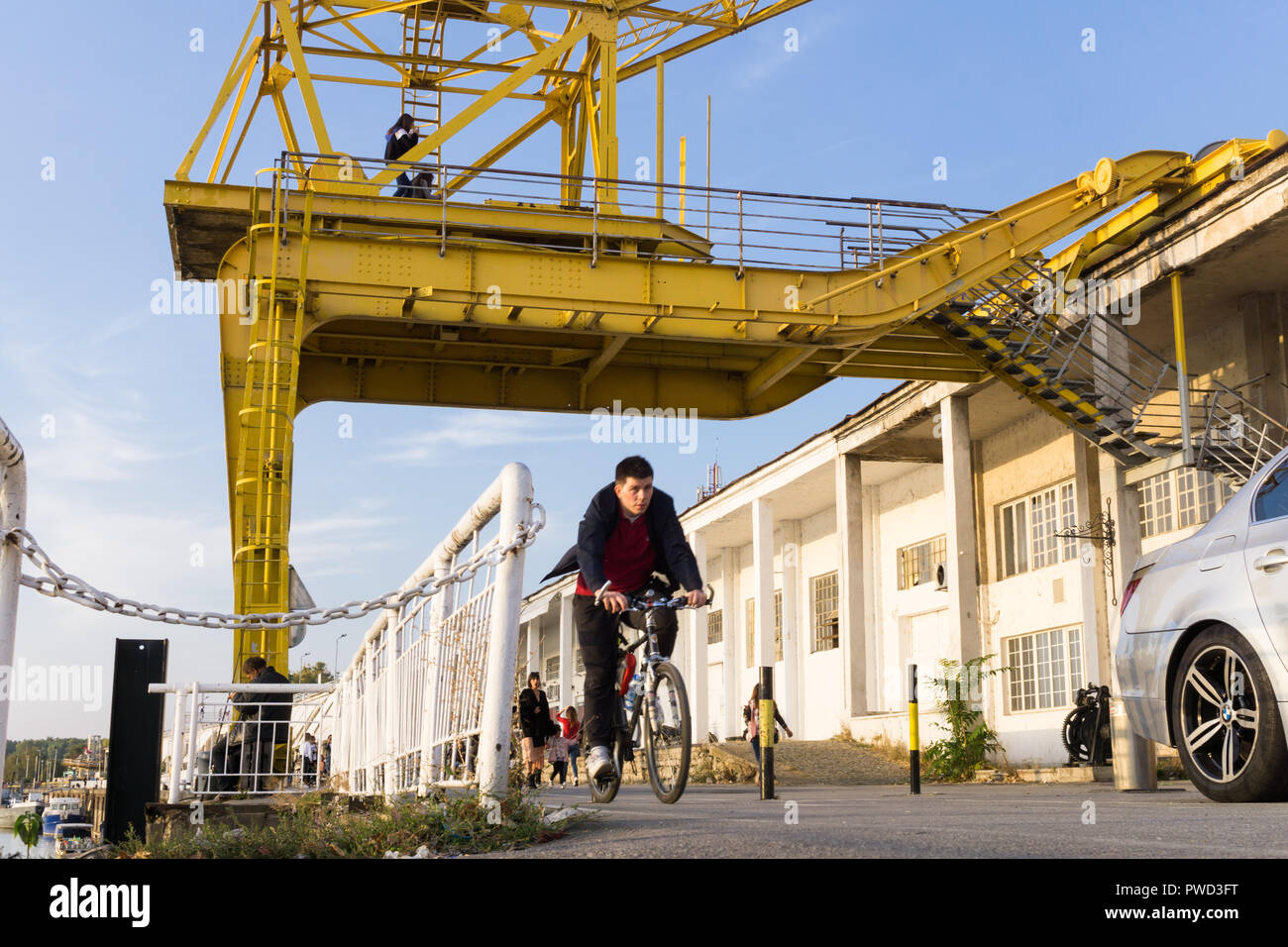 Man cycling along the bicycle path on the Sava River waterfront passing the yellow crane of the Belgrade Port. Stock Photo
