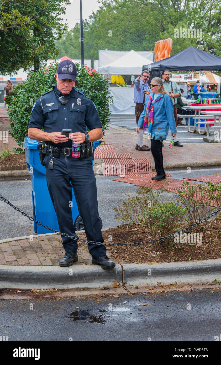 HICKORY, NC, USA-10/14/18: A local policeman on duty at fall festival, looking at his smartphone. Stock Photo