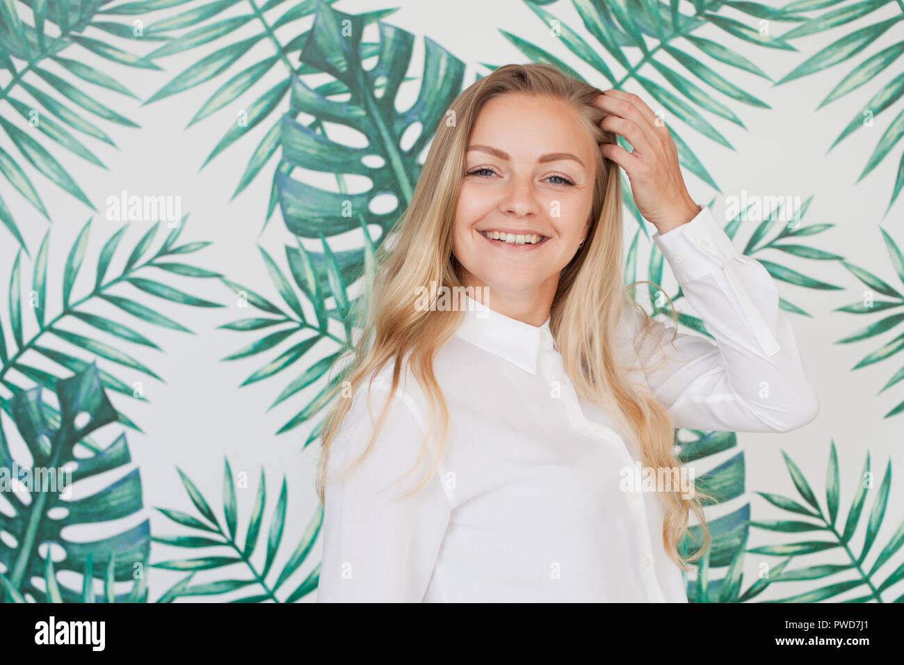 Cute young blonde woman in white shirt on wall background with pattern