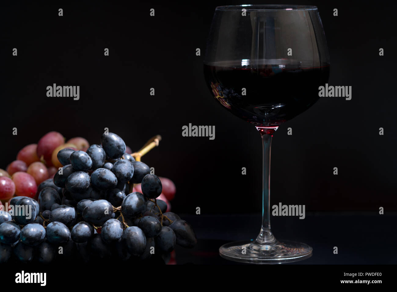 Glass of red wine alongside bunches of fresh grapes over a dark ...