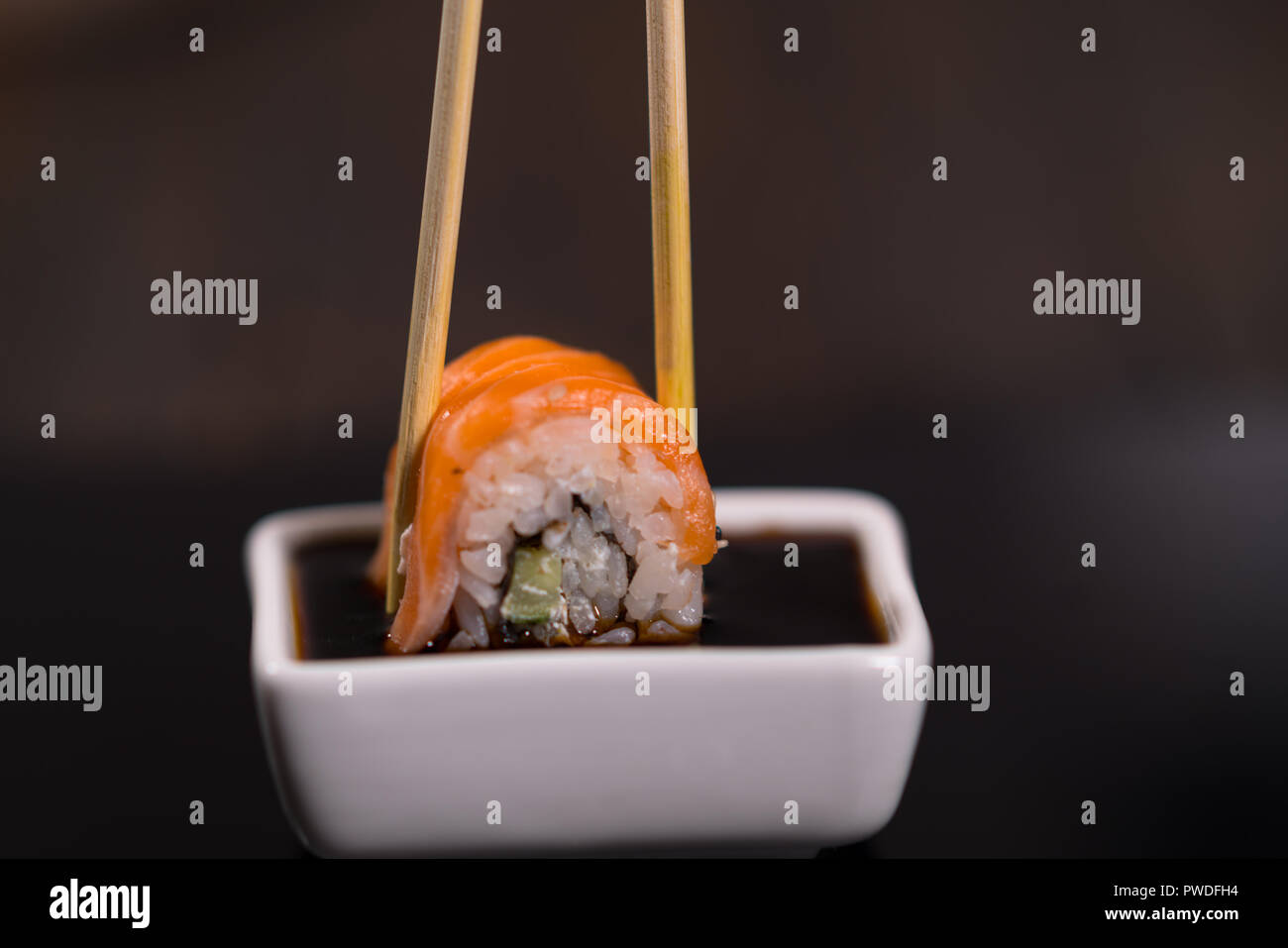 Person dipping a fresh salmon sushi roll in a small dish of soy sauce