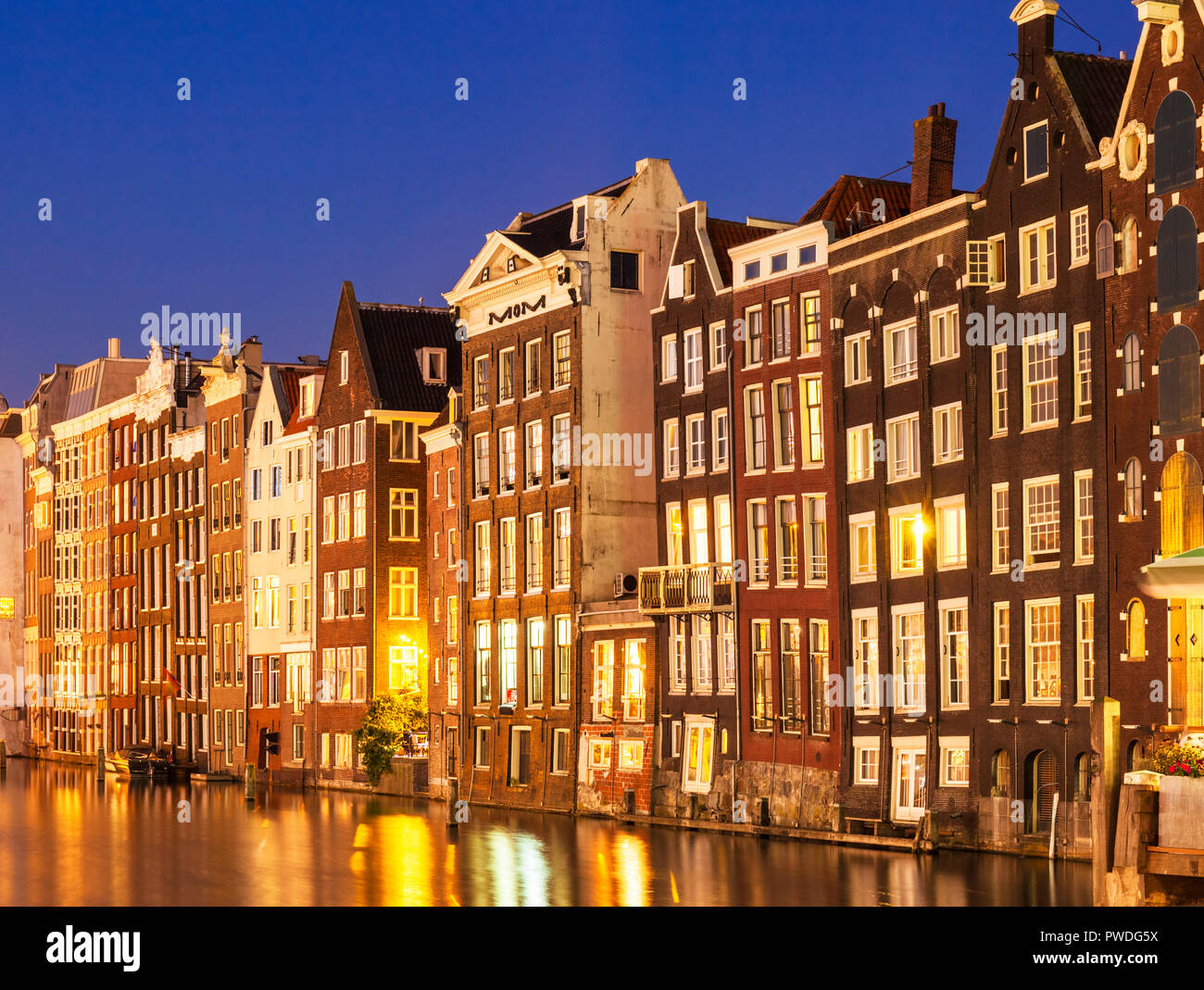 Amsterdam houses on Damrak illuminated lit up at night houses with dutch architecture by the canal Amsterdam Holland Netherlands EU Europe Stock Photo