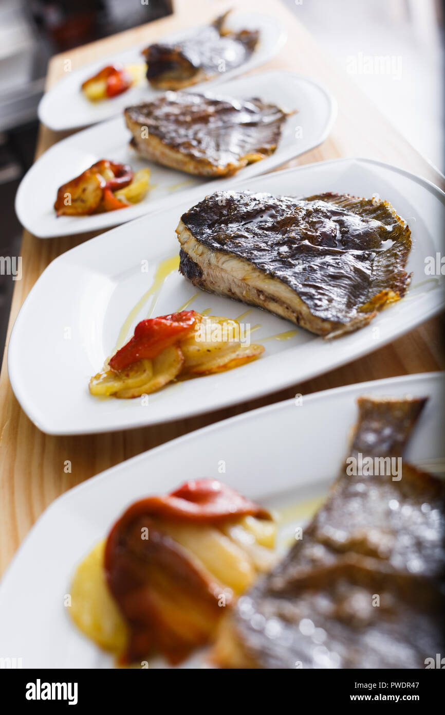 Row of white plates with piece of fried flounder on wooden tabletop in fish restaurant Stock Photo