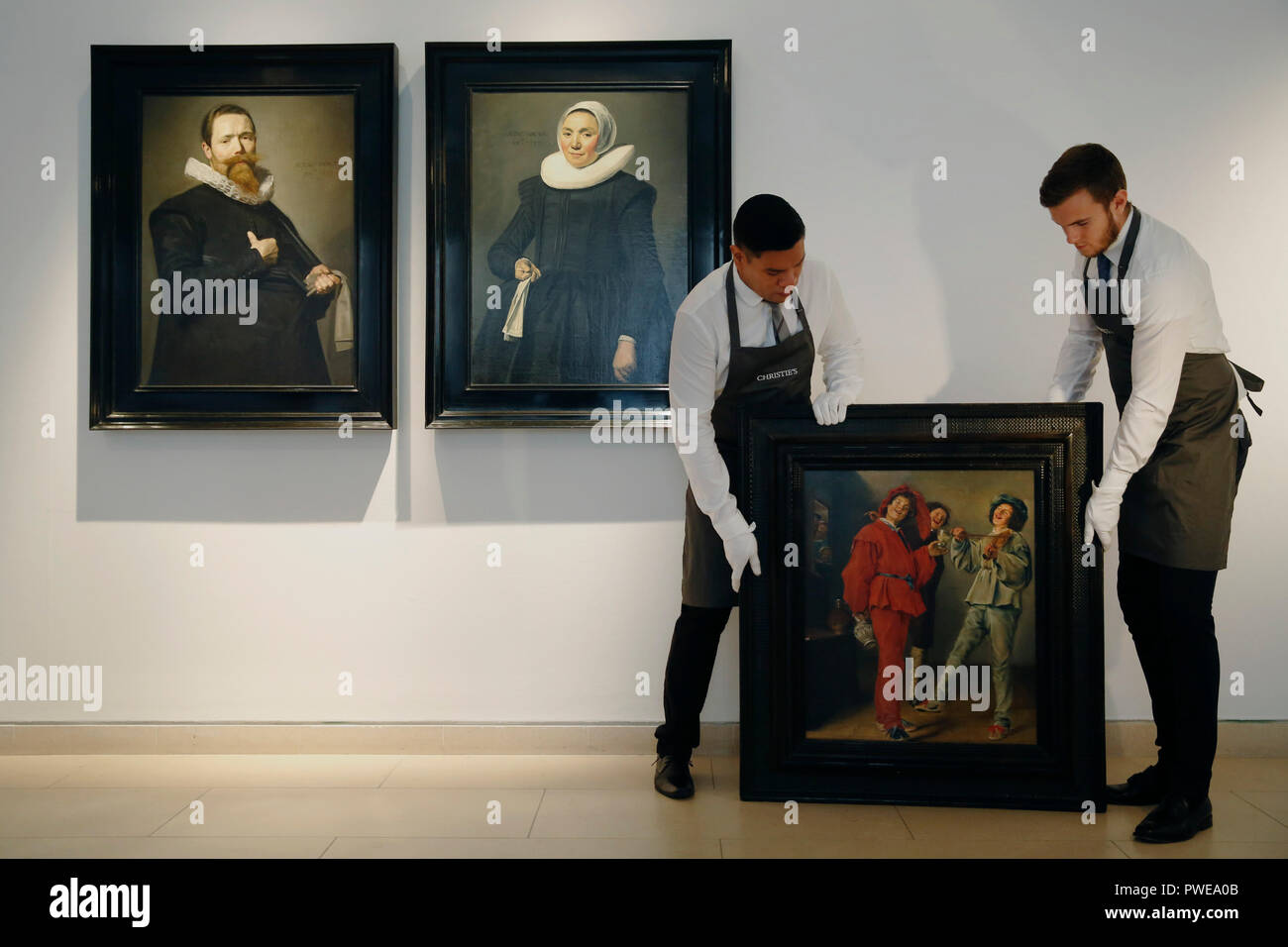 London, UK, 16th Oct 2018. Christie's art handlers hold Judith Leyster 's artwork 'Merry Company' also pictured (left) Frans Hals 's works 'Portrait of a Gentleman holding a pair of gloves' and ' Portrait of a lady holding a handkerchief' at Christie's Auction House in London, UK, Tuesday October 16, 2017. The pieces are expected to achieve up to £2.5million and £12million for the pair respectively when they come to auction as part of the Albada Jelgersma Collection sale during Christie's Classic Week in December. Photograph : Credit: Luke MacGregor/Alamy Live News Stock Photo