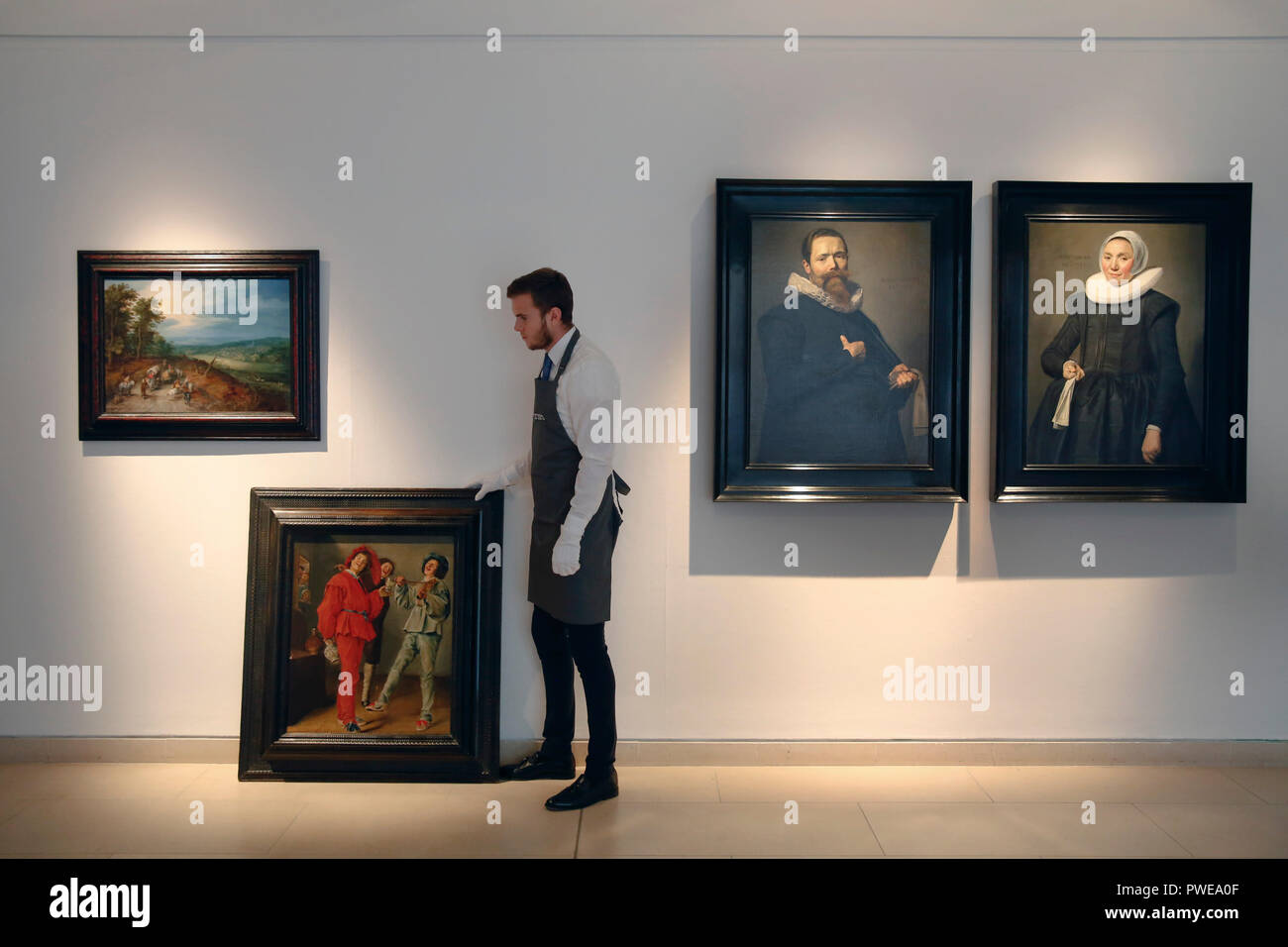 London, UK, 16th Oct 2018. A Christie's art handler stands with artworks by Dutch masters, (L-R) Jan Breughel the Elder 's 'An extensive wooded landscapef'; Judith Leyster 's 'Merry Company'; Frans Hals 'Portrait of a Gentleman holding a pair of gloves' and ' Portrait of a lady holding a handkerchief' at Christie's Auction House in London, UK, Tuesday October 16, 2017. The pieces are expected to achieve £5million, £2.5million and £12million for the pair respectively when they come to auction as part of the Albada Jelgersma Collection sale during Christie's Classic Week in December. Photograph  Stock Photo