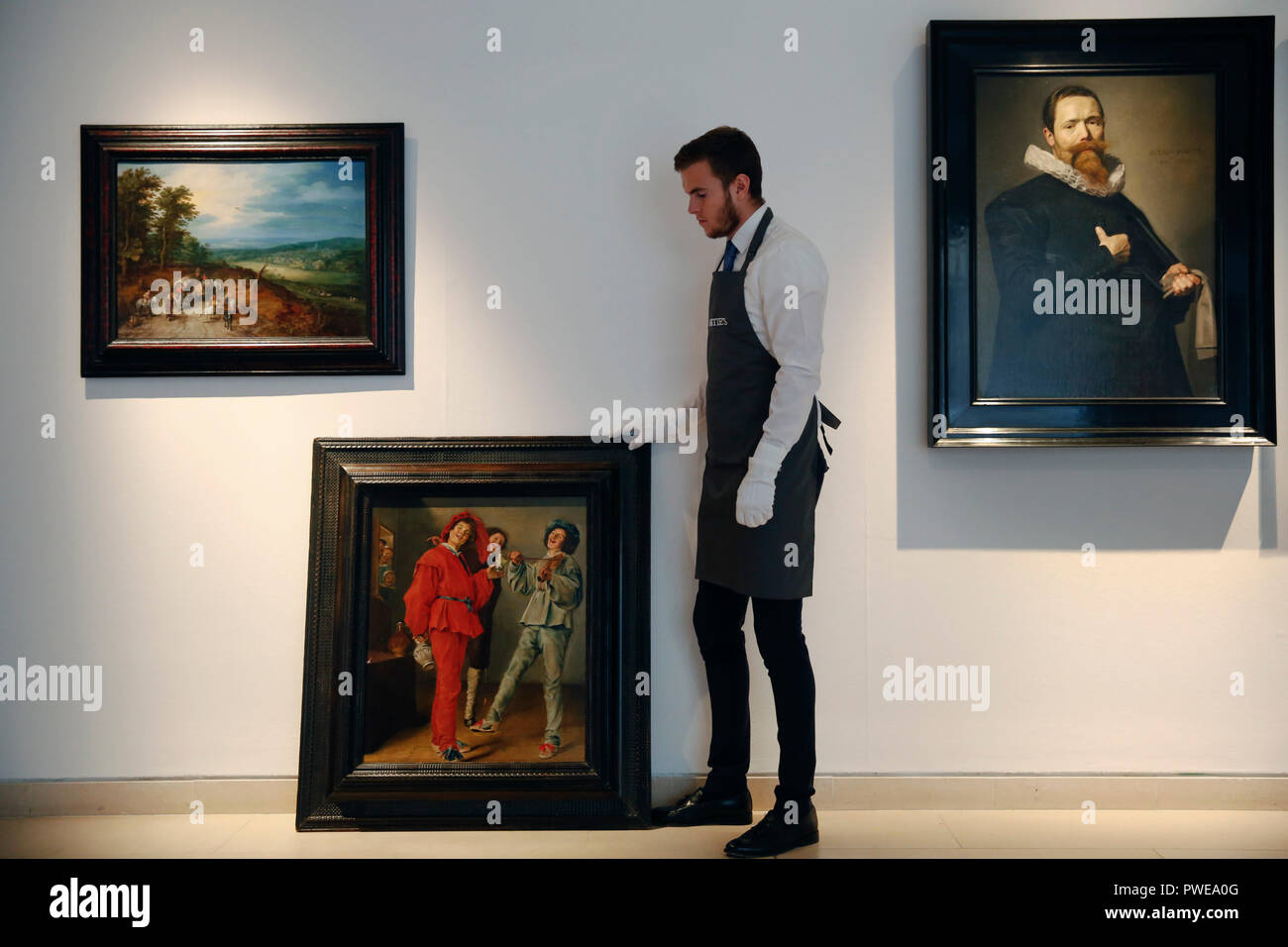 London, UK, 16th Oct 2018. A Christie's art handler stands with artworks by Dutch masters, (L-R) Jan Breughel the Elder 's 'An extensive wooded landscapef'; Judith Leyster 's 'Merry Company'; Frans Hals 'Portrait of a Gentleman holding a pair of gloves' a at Christie's Auction House in London, UK, Tuesday October 16, 2017. The pieces are expected to achieve £5million, £2.5million and £12million ( one of a pair ) respectively when they come to auction as part of the Albada Jelgersma Collection sale during Christie's Classic Week in December. Photograph : Credit: Luke MacGregor/Alamy Live News Stock Photo