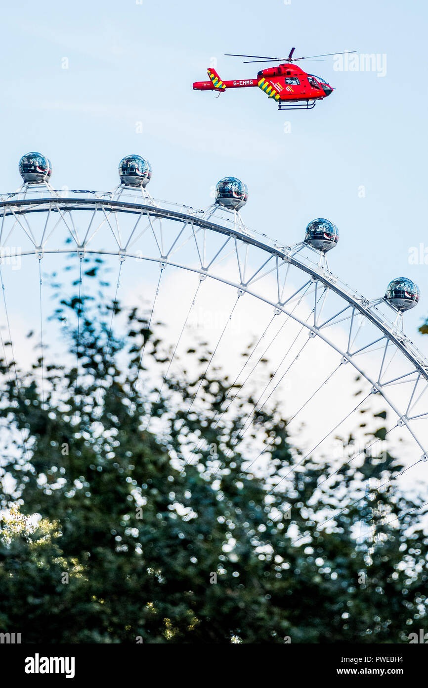 London, UK. 16th October, 2018. The Air Ambulance takes off between St James Park and Whitehall and rises past the tourists on the London Eye after a road accident in Westminster. Credit: Guy Bell/Alamy Live News Stock Photo