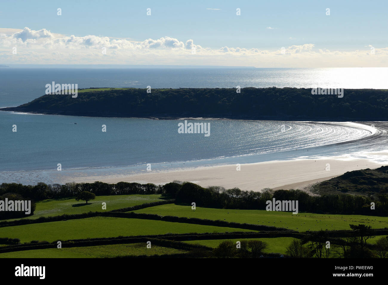 Bright sunshine over the sweeping bay of Oxwich and Crawley woods with the Bristol channel and distant Devon visible under distant  puffy white clouds Stock Photo