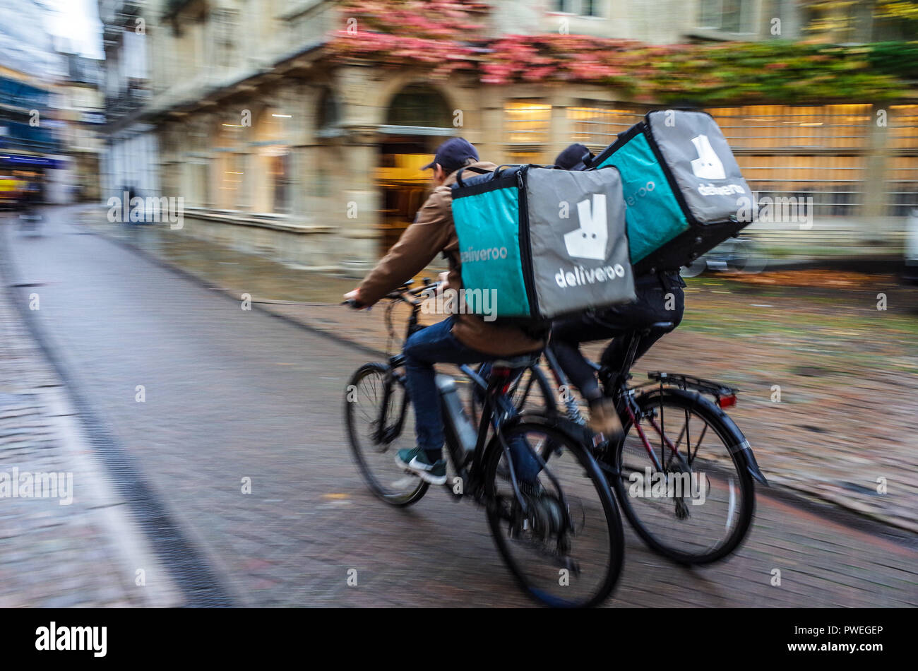 Deliveroo Riders Gig Economy - two Deliveroo Food Delivery Couriers ride through central Cambridge Stock Photo