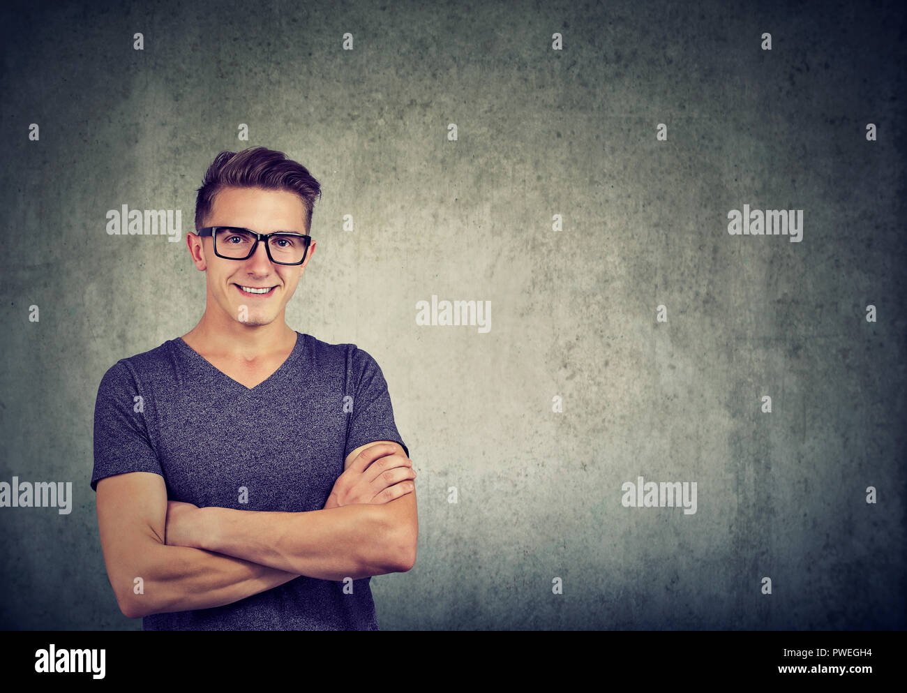 Young casual man with arms crossed wearing glasses and looking smart on gray background Stock Photo