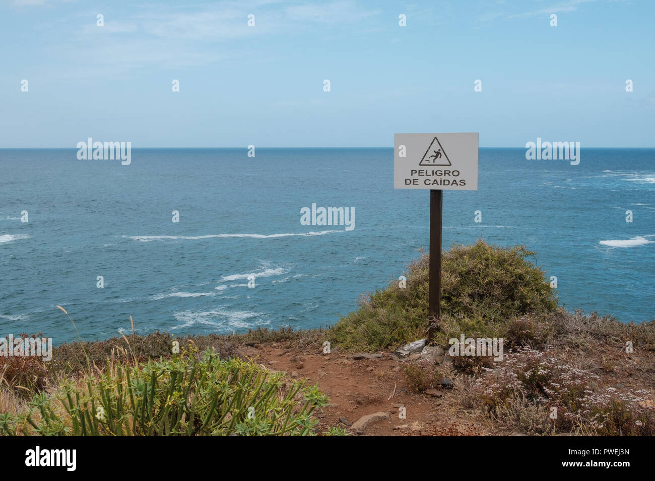 fall hazard (spanish: Peligro De Caidas) warning sign with ocean landscape background Stock Photo