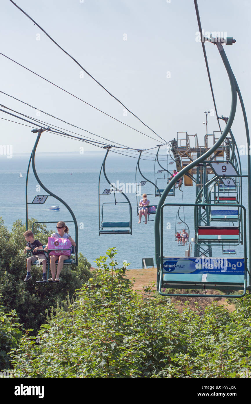 People on the Chairlift overlooking Alum Bay, and The Needles, Isle of Wight. Hampshire. Southern England. The UK. Empty seats, occupied seats. Summer. Stock Photo