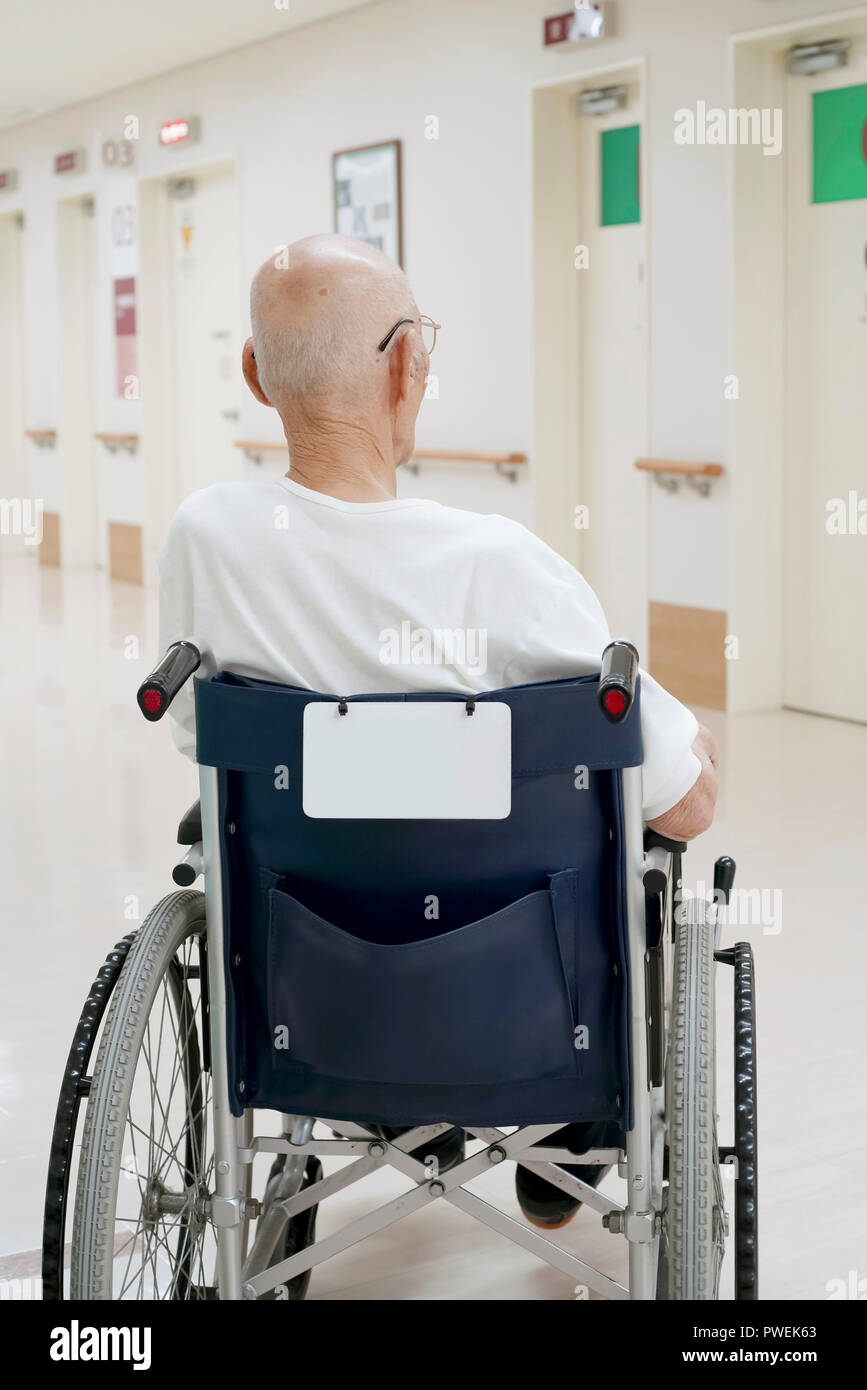 Back view of old man sitting on wheelchair in hospital hallway Stock Photo