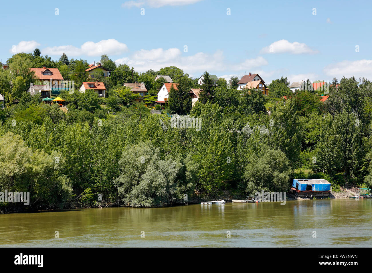 Hungary, Mohacs on the Danube, Transdanubia, Southern Transdanubia, Baranya county, residential buildings on a hill above the Danube, single-family houses, river bank, river landscape, trees and bushes at the Danube bank, cumulus clouds Stock Photo