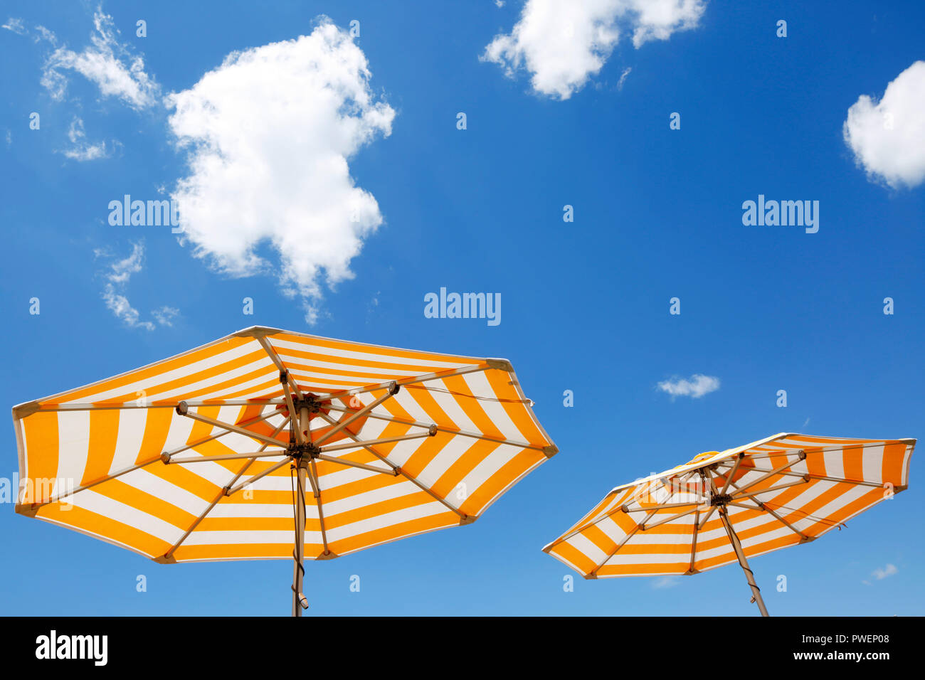 two parasols on a cruise ship against the blue sky, yellow and white, cumulus clouds, holiday, freetime, recreation, relaxation, sunlight, sunshine, shelter from sun, unpeopled, travel, cruise, tourism Stock Photo