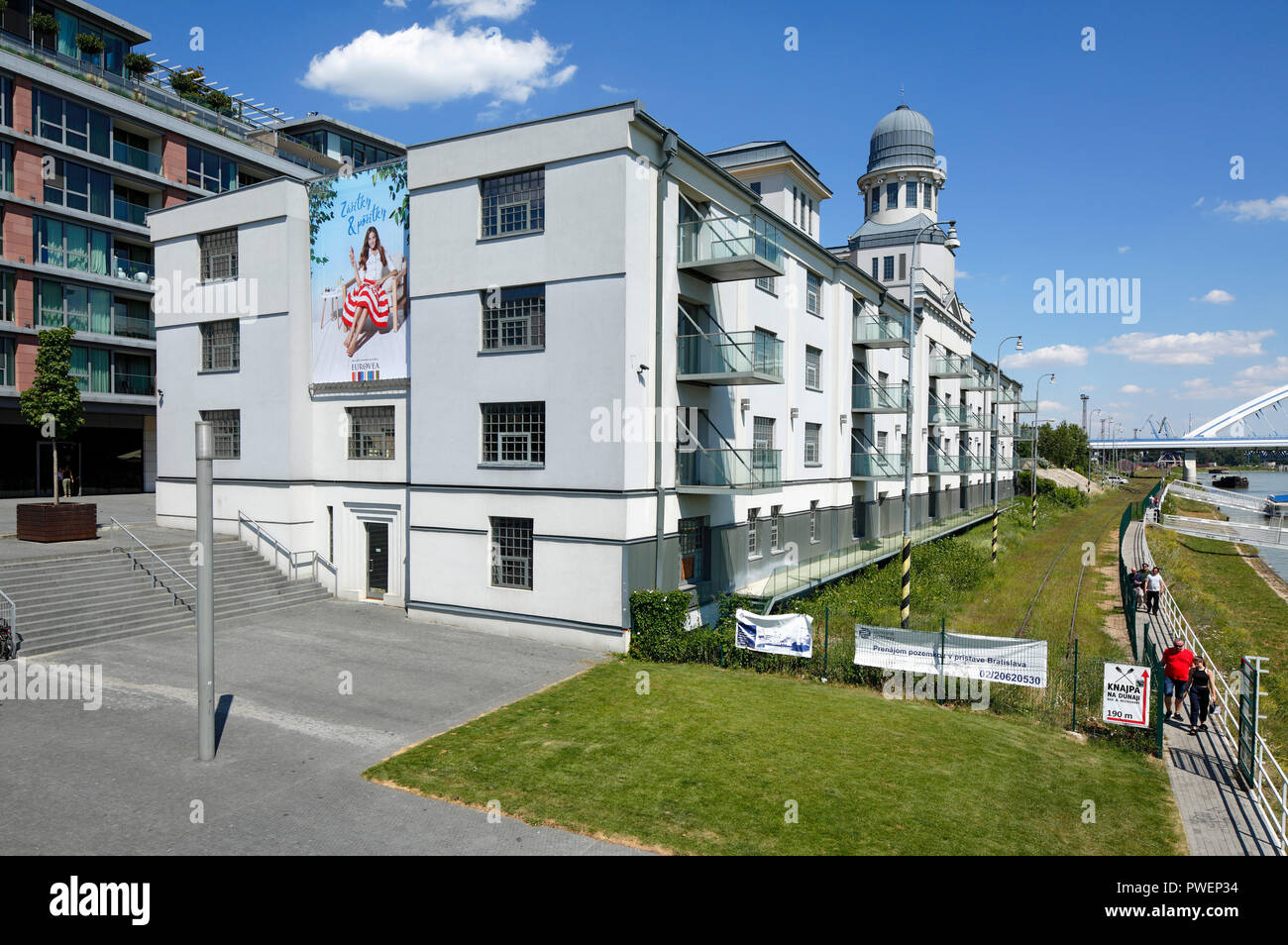 Slovak Republic, Slovakia, Bratislava, Capital City, Danube, Little Carpathians, residential building at the Danube riverbank, multi-family house, multipurpose building, Danube riverwalk, protective wall, shipping pier, gangway, people stroll along a towpath Stock Photo