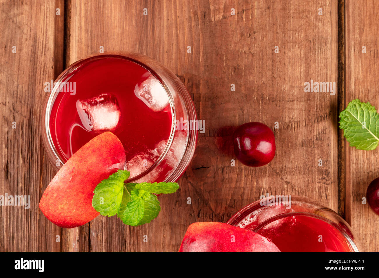 A photo of vibrant red drinks with cherries, shot from the top on a dark wooden background with a place for text Stock Photo
