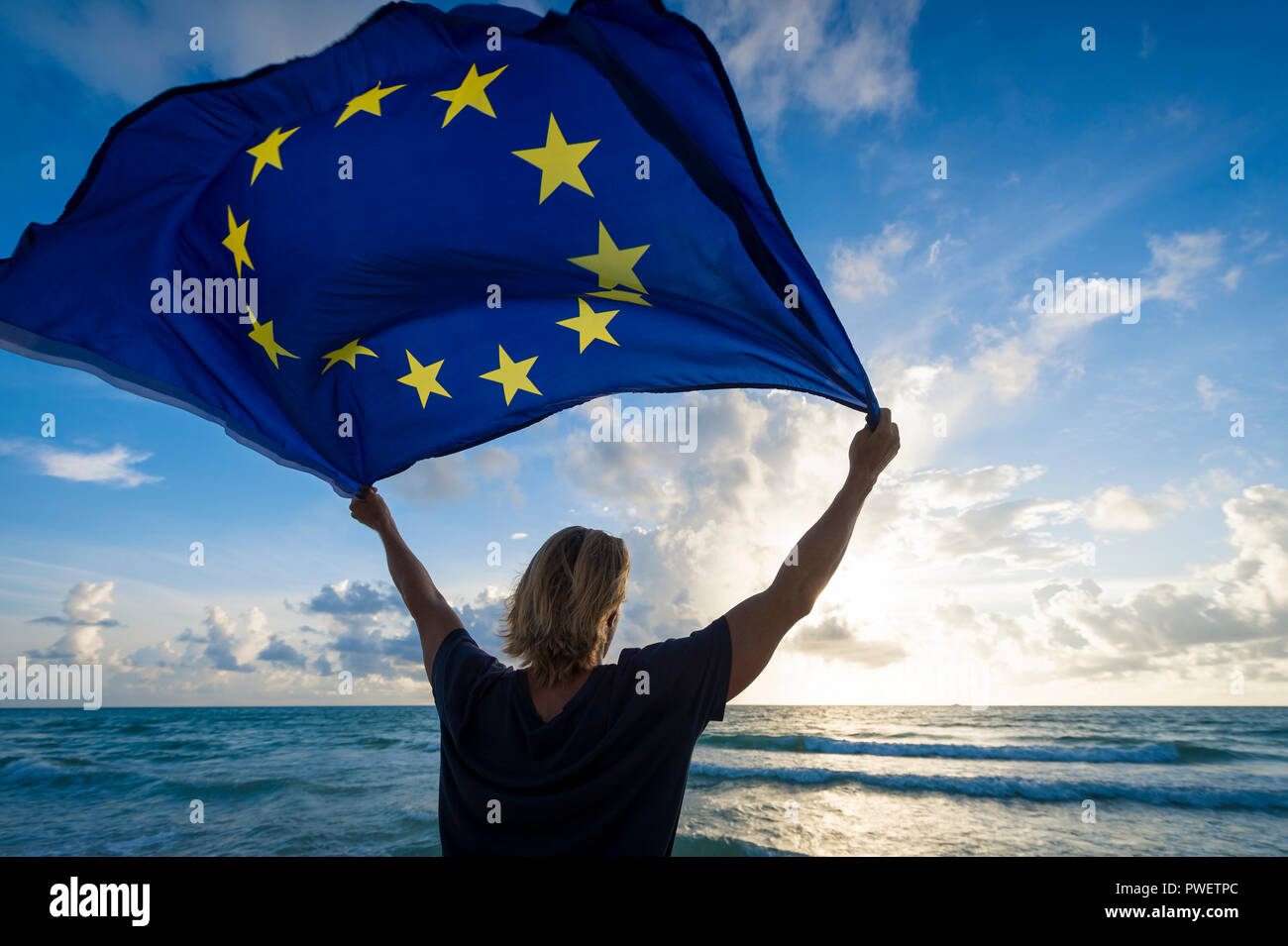 Silhouette of person holding European Union flag against soft sunset sky Stock Photo