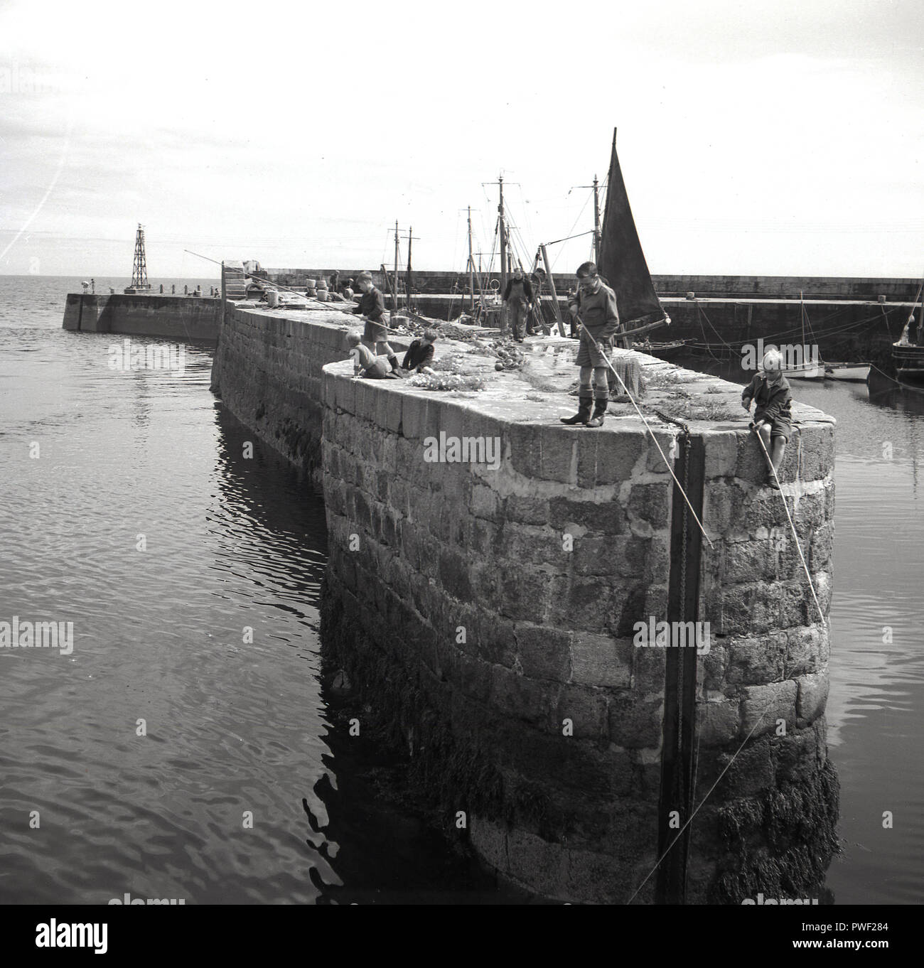 1950s, historical, young children fishing from a sea wall, in a harbour in Northern Ireland, UK. In this era, children had a great deal of freedom to play outside on their own and as can be seen in this picture, a group of boys are happily fishing from a high wall into deep water below without any adult supervision. Stock Photo