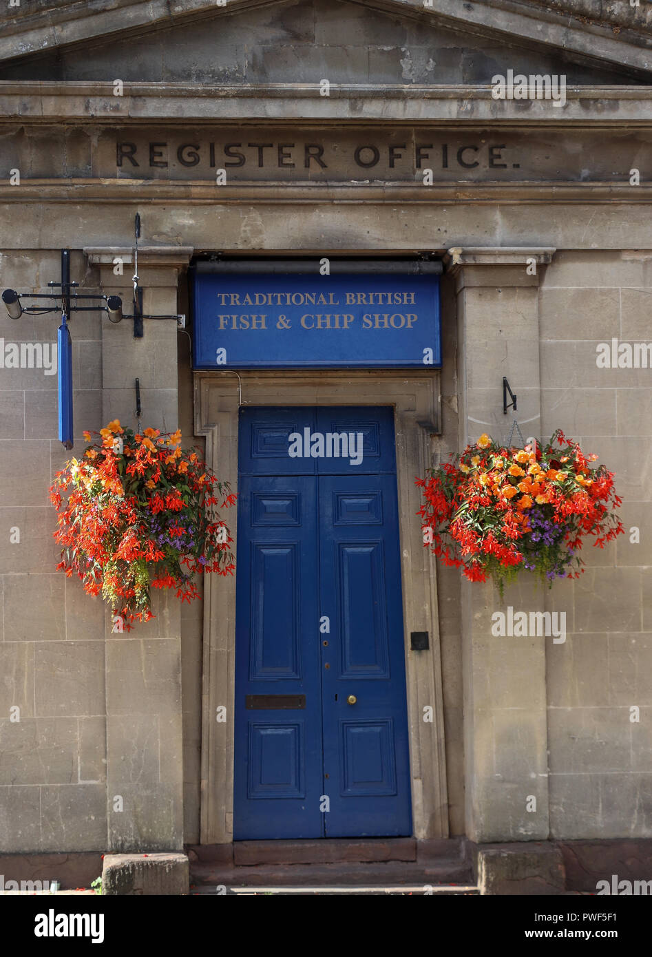 An old Register Office in Thornbury, Gloucestershire, UK is now a fish and chips shop with a bright blue door and two colorful hanging flower baskets Stock Photo