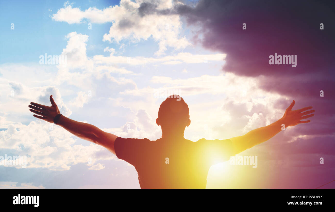 Young man standing with arms outstretched at sunset Stock Photo