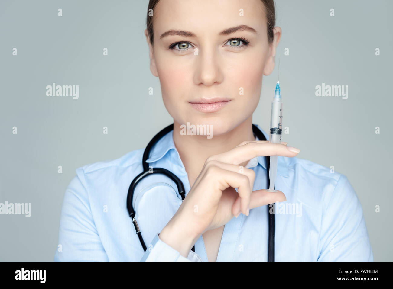 Portrait of a serious woman doctor with syringe in hand isolated on gray background, injections, plastic surgery and beauty treatments concept Stock Photo