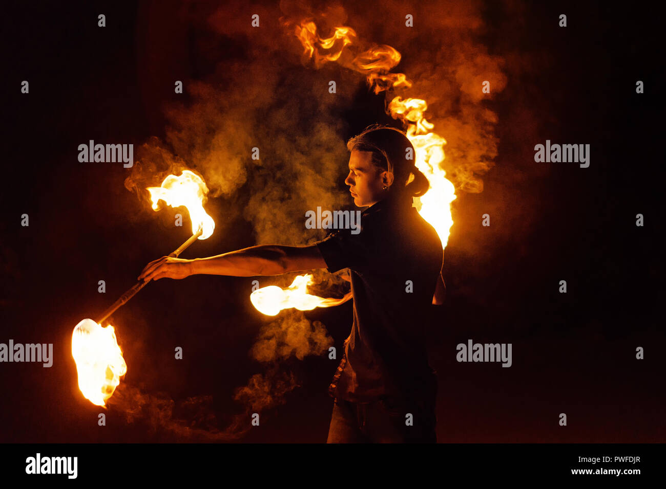 Fire show. Fire dancer dances with two Staff. Night performance. Dramatic portrait. Fire and smoke. A fascinating movement of the flame. Stock Photo