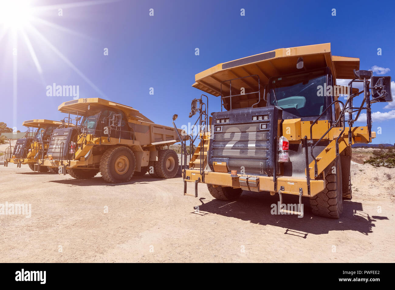 Large yellow industrial dumper trucks on construction site with sun