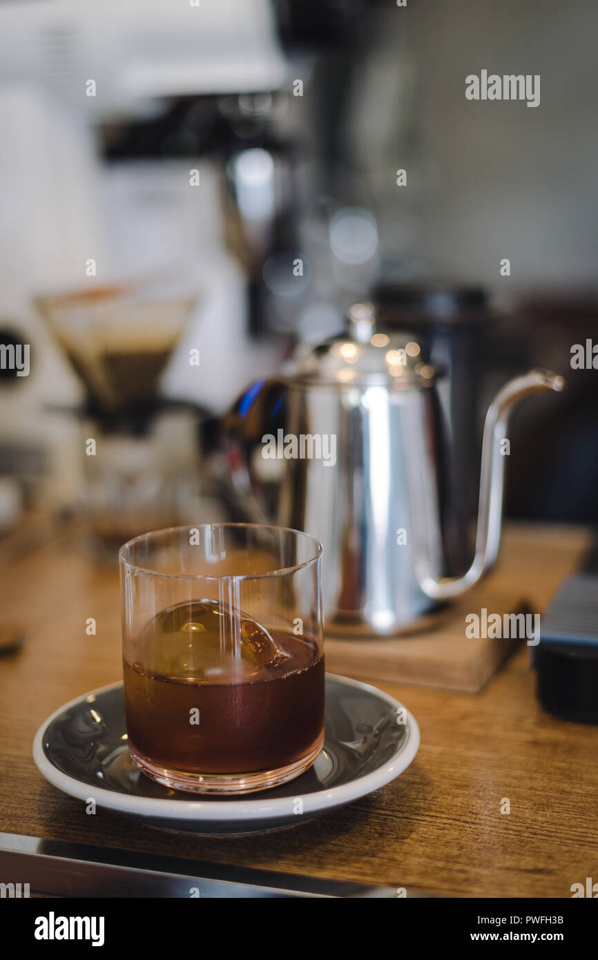 Iced drip coffee with ice ball in glass with blur coffee bar scene