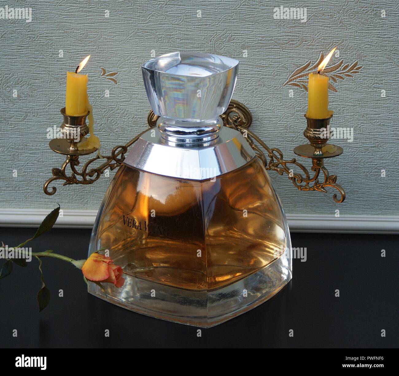 Vera Wang, fragrance for ladies, large perfume bottle in front of a piano candelabra with shining candles decorated with an English rose Stock Photo