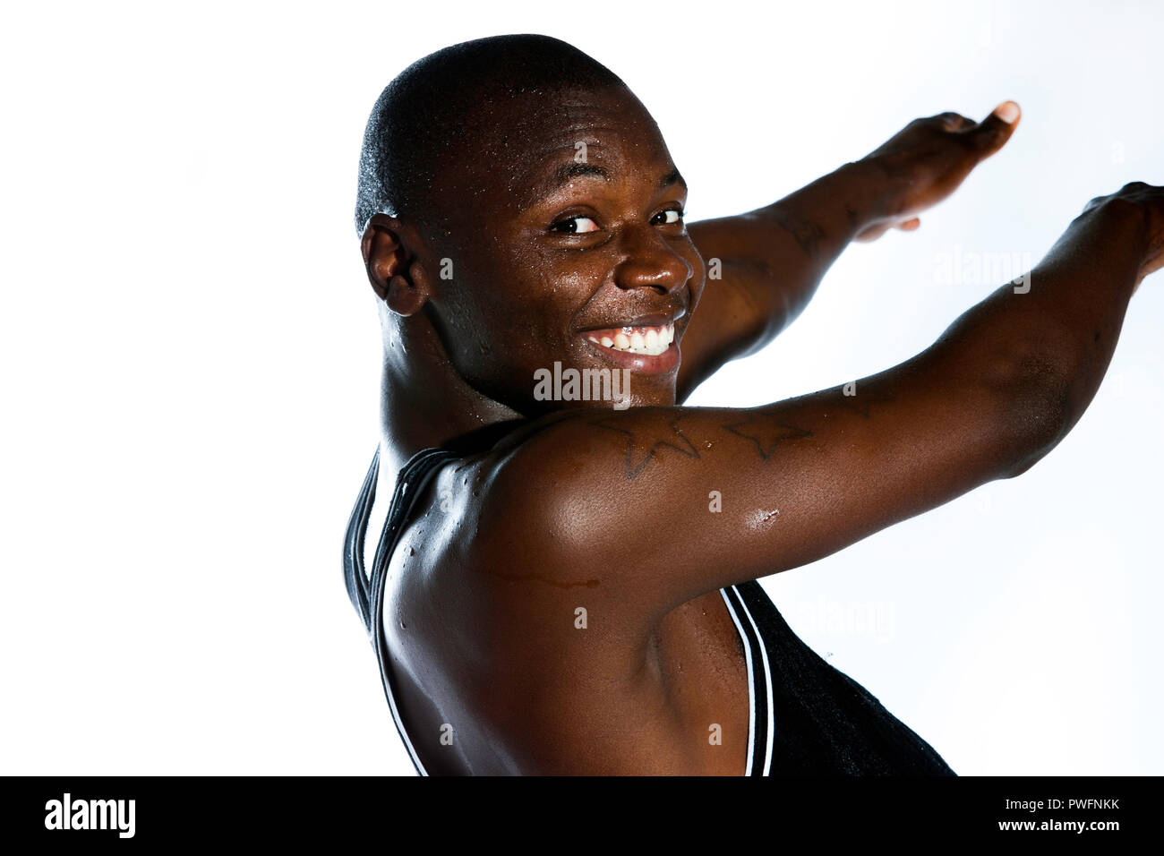 Handsome young african male dancing and smiling backwards at the camera with a wet face and water drops on his arms. Showing three prison tattoos Stock Photo