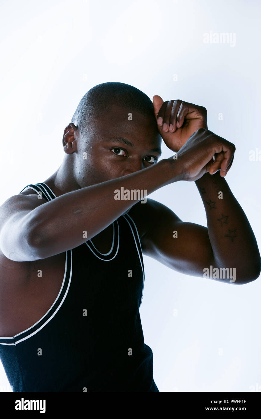 Young african male in a defensive pose, with his hands in a self protecting gesture in front of his face. Prison tattoos on his arm Stock Photo