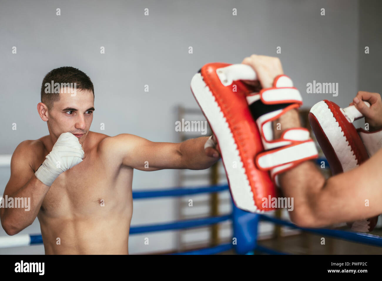 Kickboxer training with partner in boxing paws, using boxing mitts. Preparing for competition