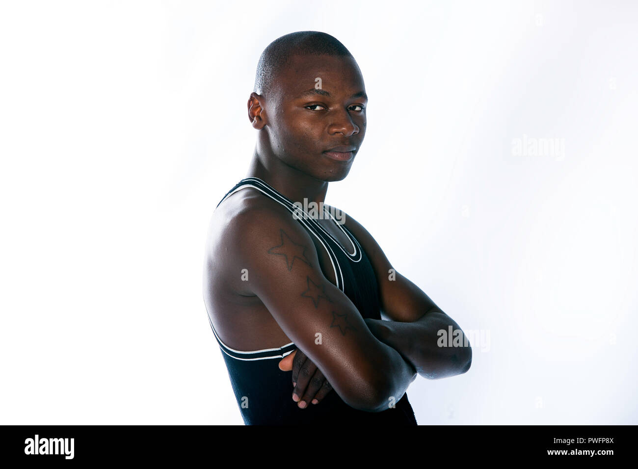 African male with three prison tattoos wearing a muscle shirt looking sideways towards the camera with his arms crossed. Stock Photo