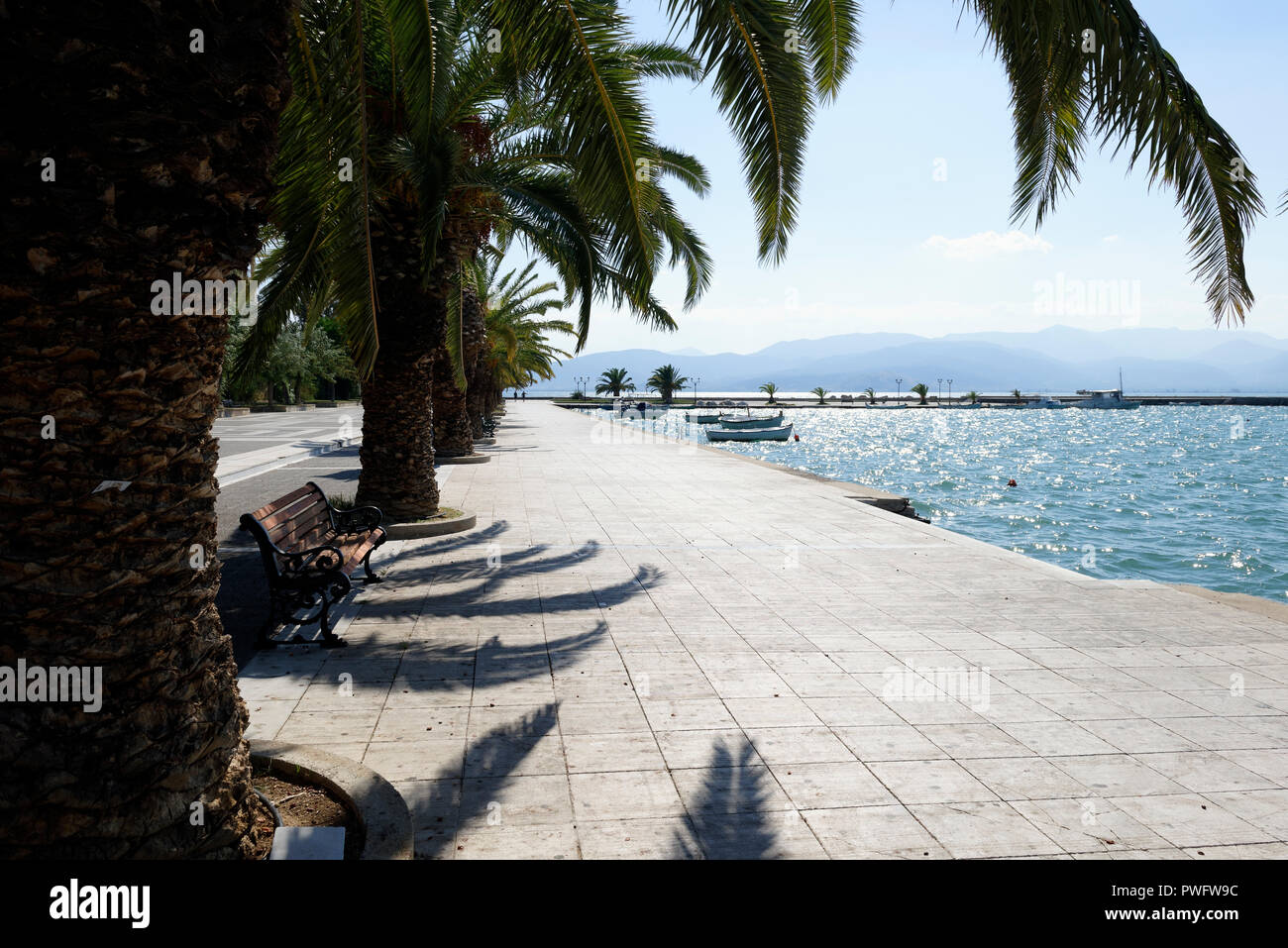 Palm trees line the waterfront and fishing boats dock in the harbour of the town of Nafplio. Peloponnese. Greece. From 1829 to 1334, the town was the  Stock Photo