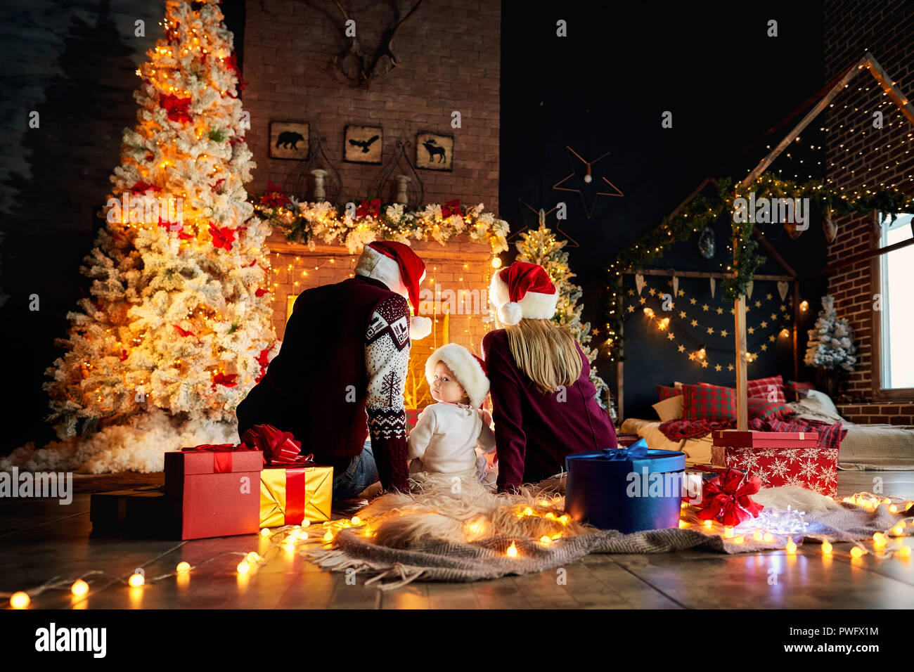 Happy family with a baby in a Santa Claus hat in a Christmas room in Christmas day. Stock Photo