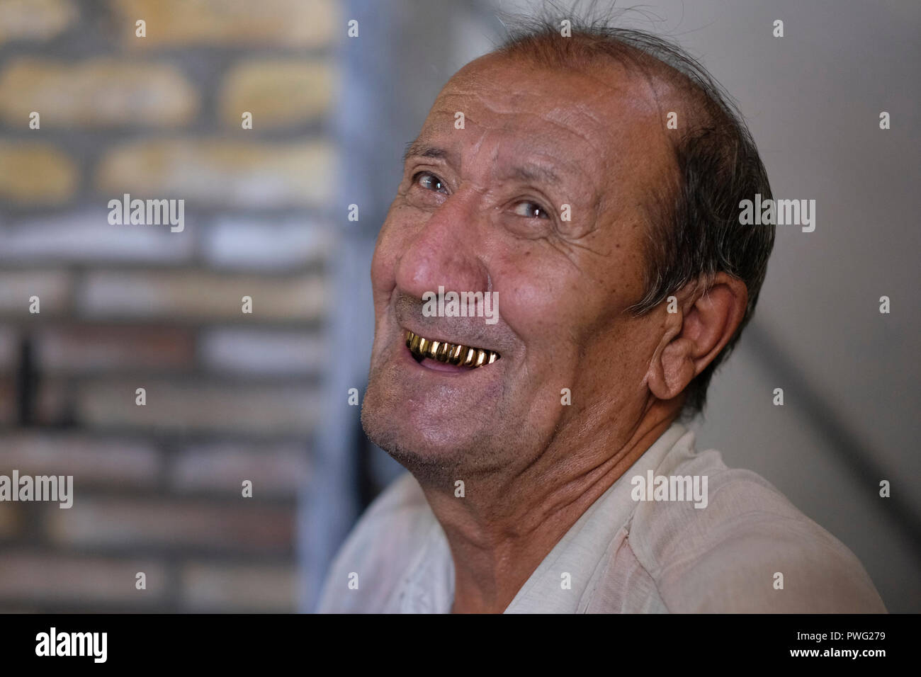 Uzbek man with gold capped teeth smiling in the historic city of Khiva the former capital of Khwarezmia and the Khanate of Khiva listed as Unesco world heritage site located in Xorazm Region, Uzbekistan. Replacing natural teeth with gold implants or caps was once a status symbol and prestige in Uzbekistan and other countries of Central Asia. Stock Photo