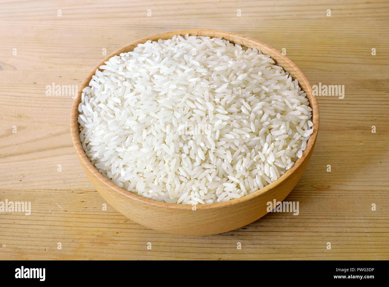 Raw, parboiled rice in a wooden bowl. Rice dish on a wooden table, diet or healthy eating scene. Stock Photo